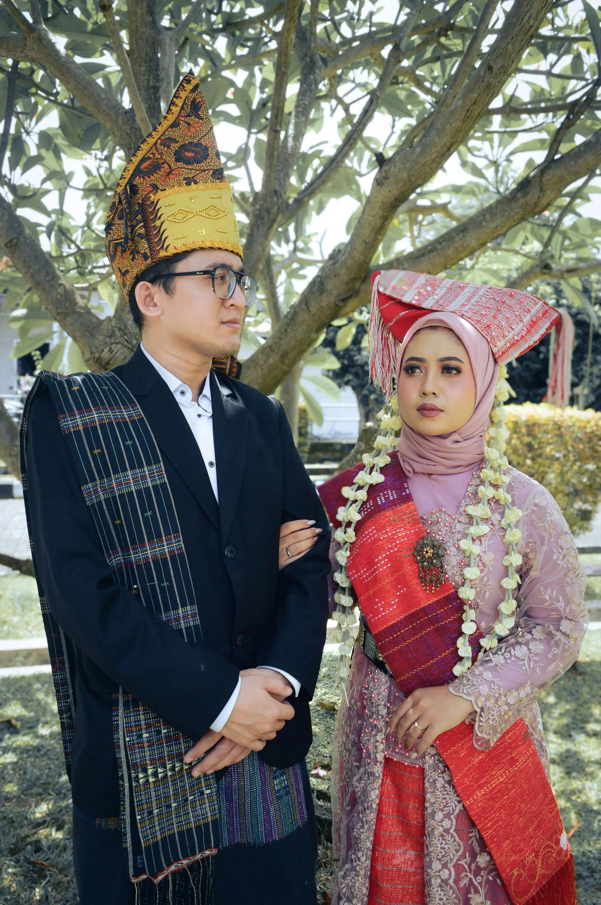 Pasangan berbusana adat dengan hiasan kepala emas dan untaian melati