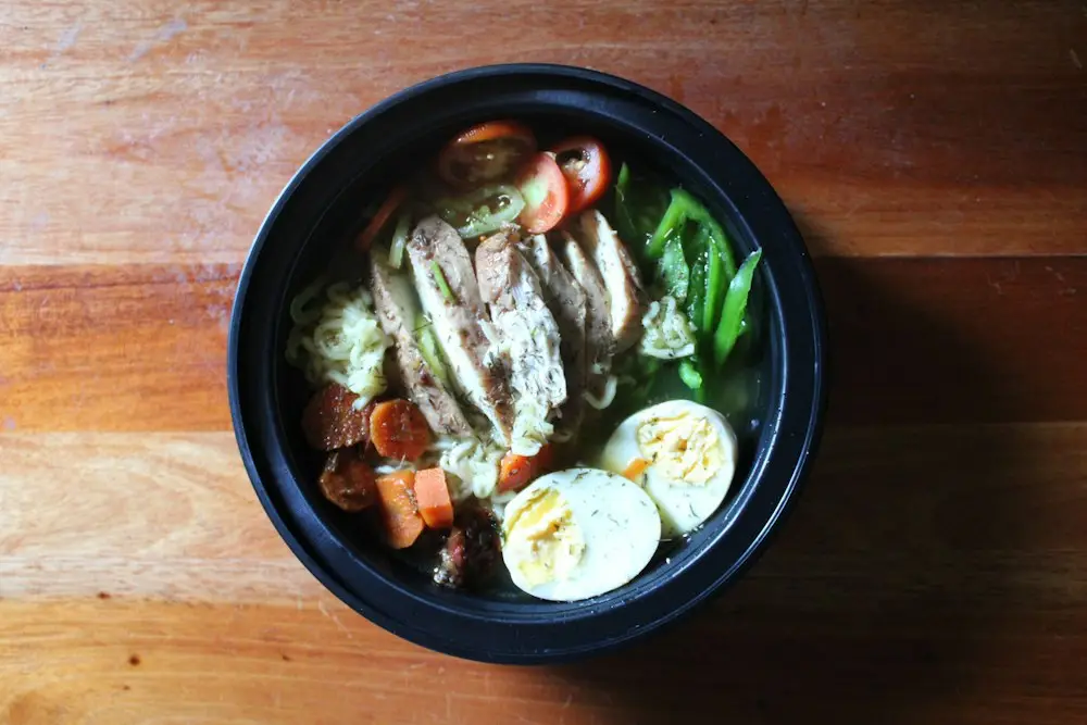 Semangkuk soto dengan ayam suwir, telur rebus, dan sayur di atas meja kayu