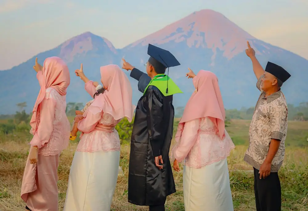 Wisudawan dan keluarganya berpose menunjuk ke arah gunung