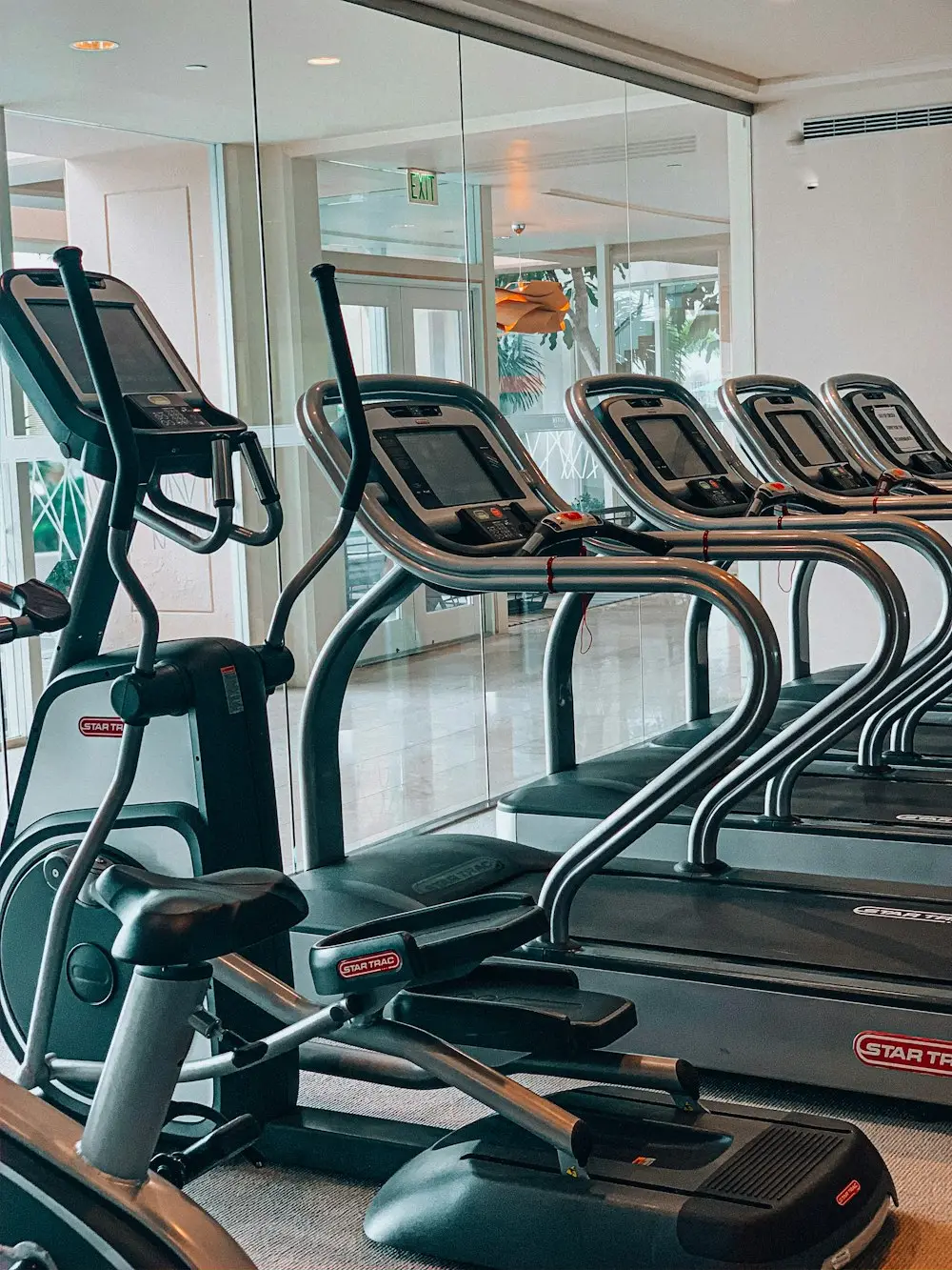 Deretan treadmill dan mesin elips menghadap dinding kaca