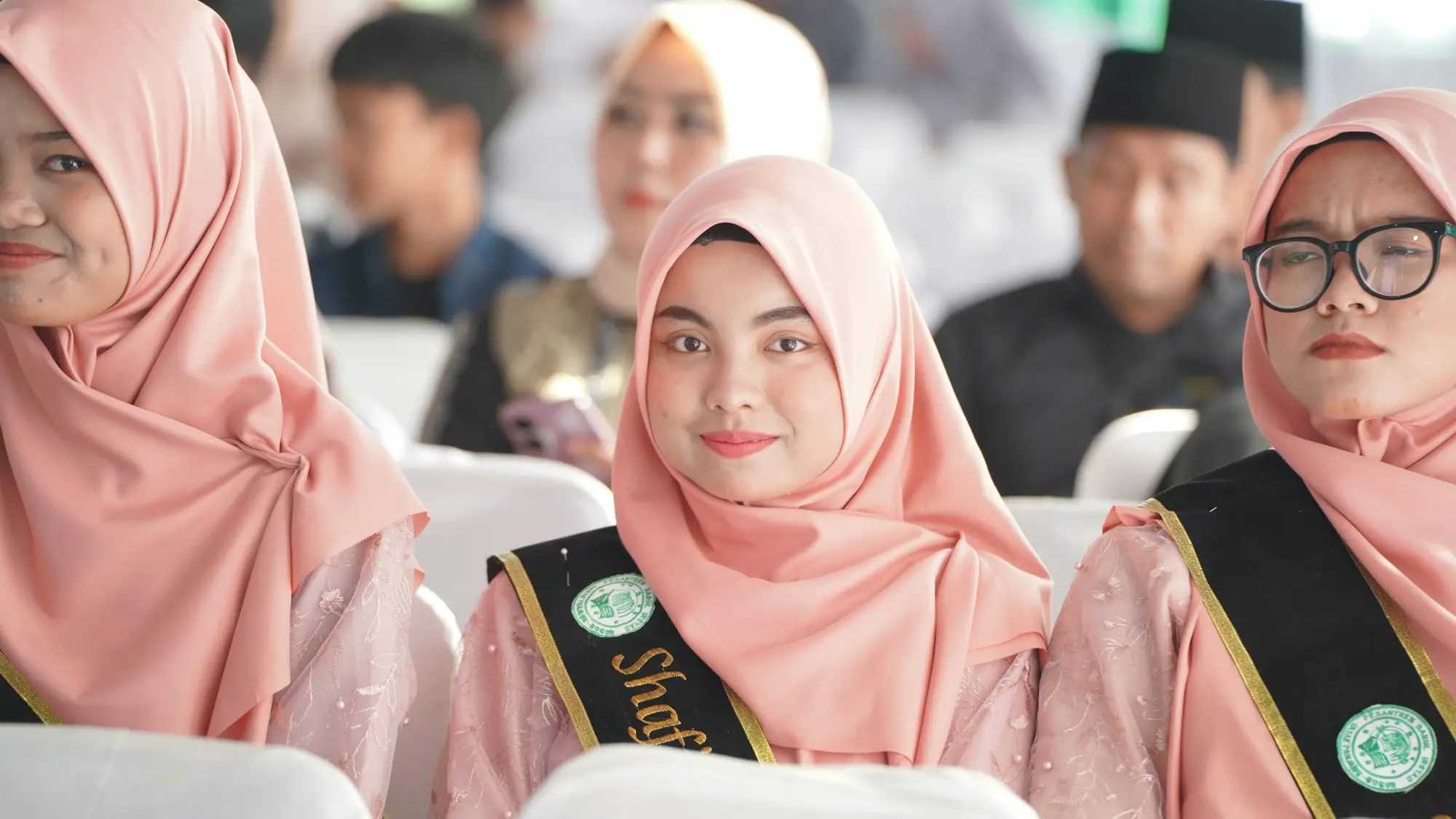 Teman seangkatan berkerudung merah muda duduk berderet di acara wisuda
