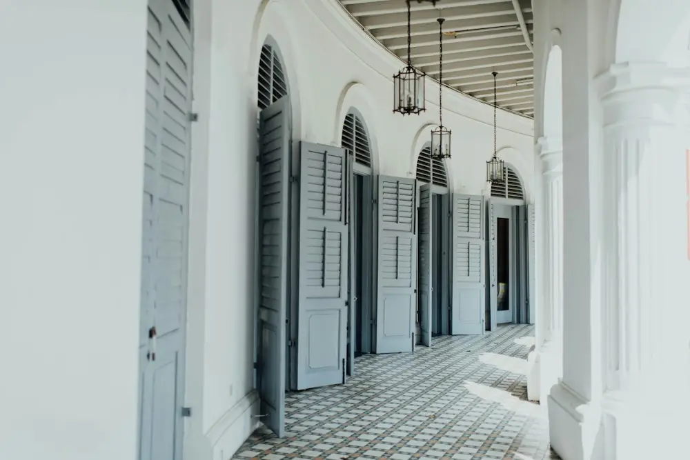 Koridor beratap dengan deretan pintu kamar dan lantai tegel bermotif