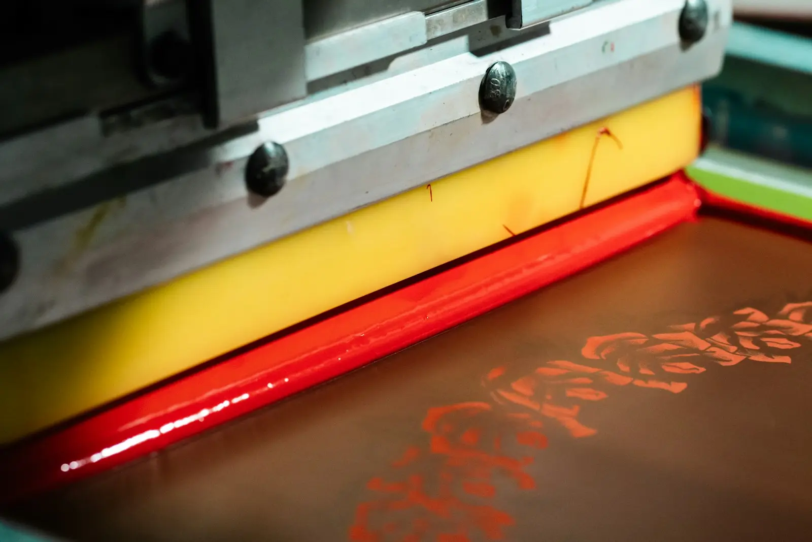 Tinta merah disapu rakel di atas screen sablon