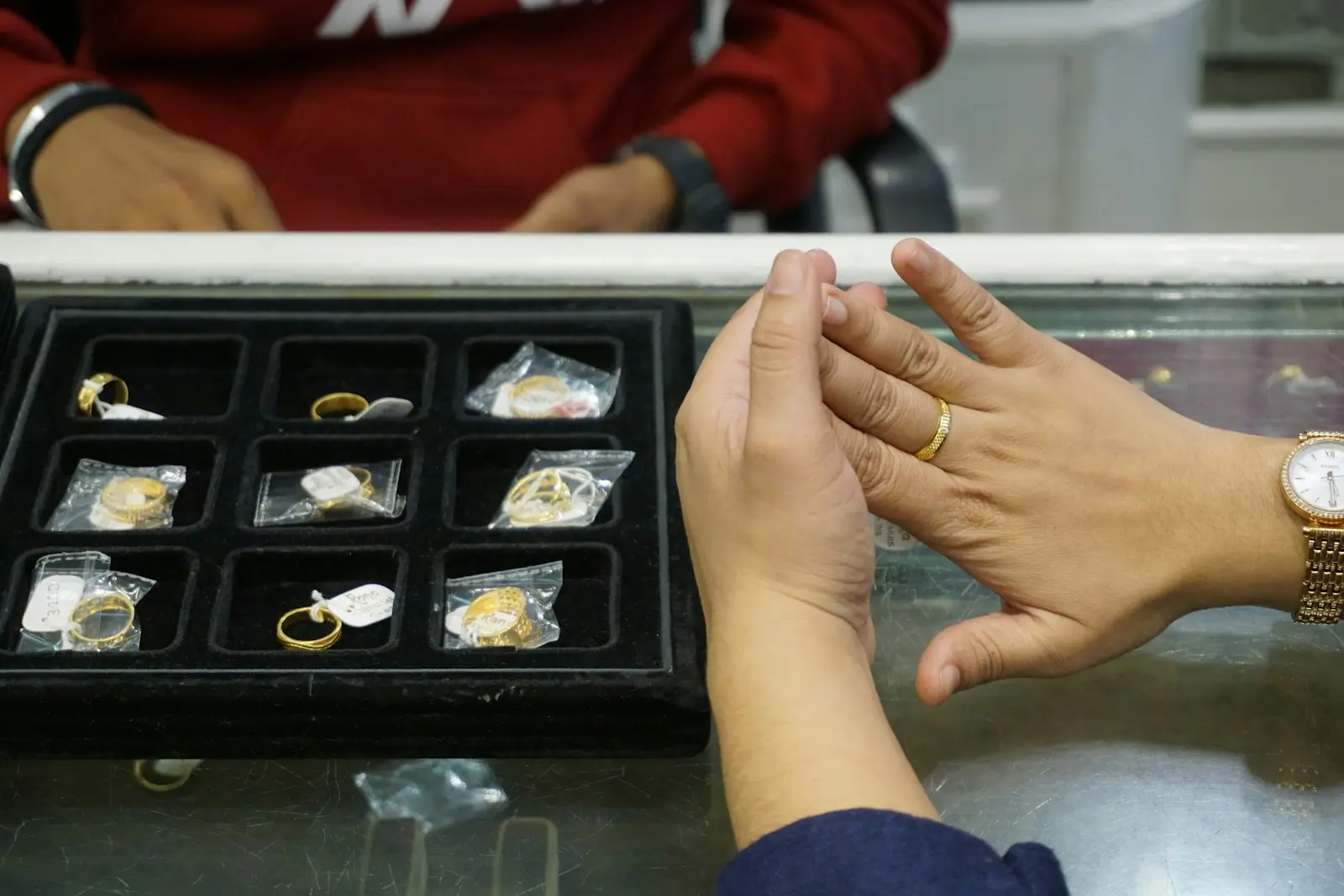 Tangan penjual dan pembeli di atas etalase berisi cincin emas