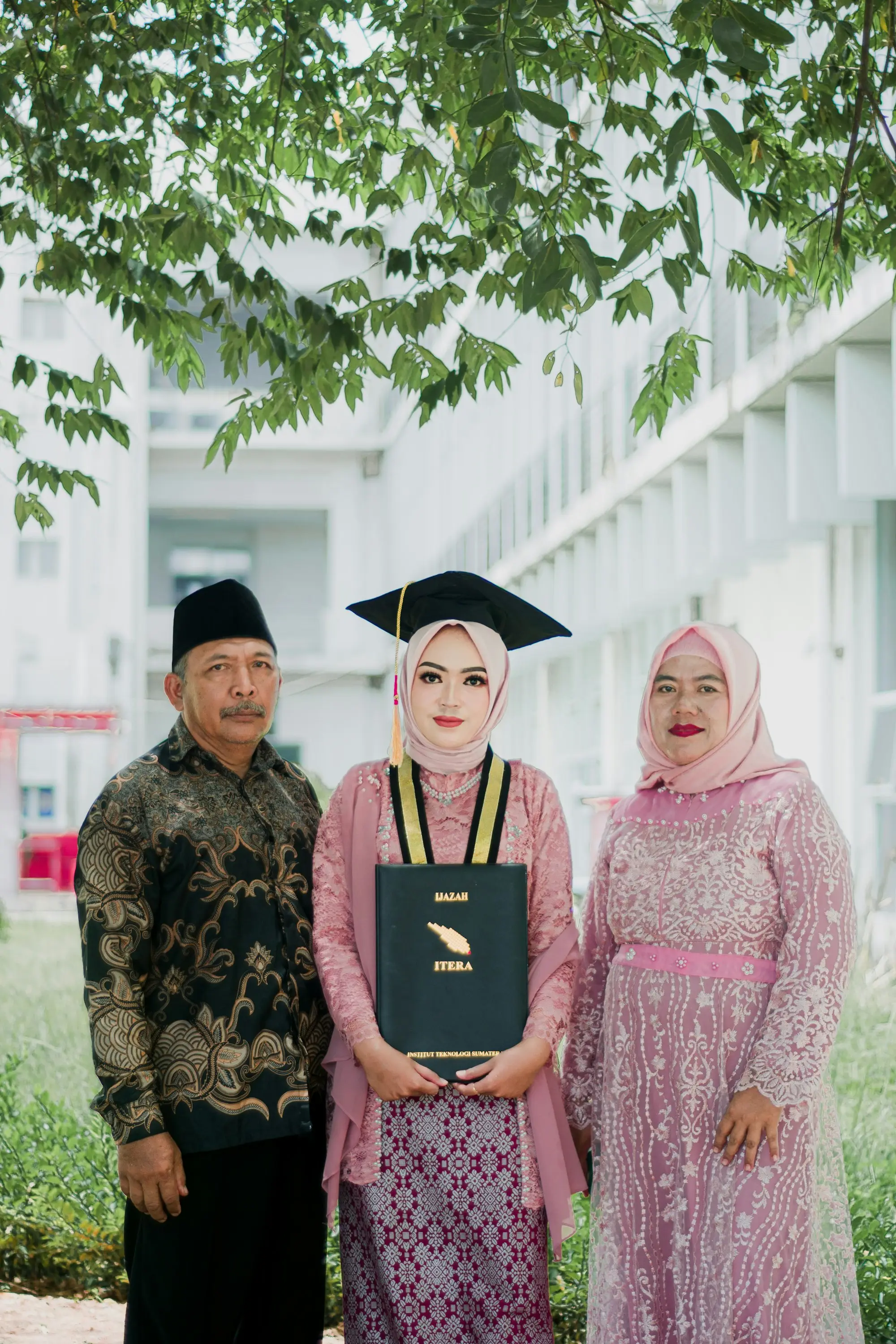 Wisudawati bersama ayah dan ibunya di depan gedung kampus