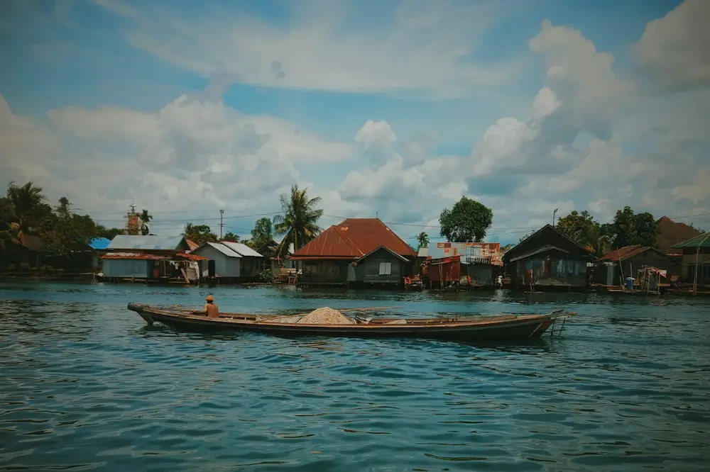 Rumah-rumah panggung berjajar di tepi sungai, sebuah perahu kayu melintas