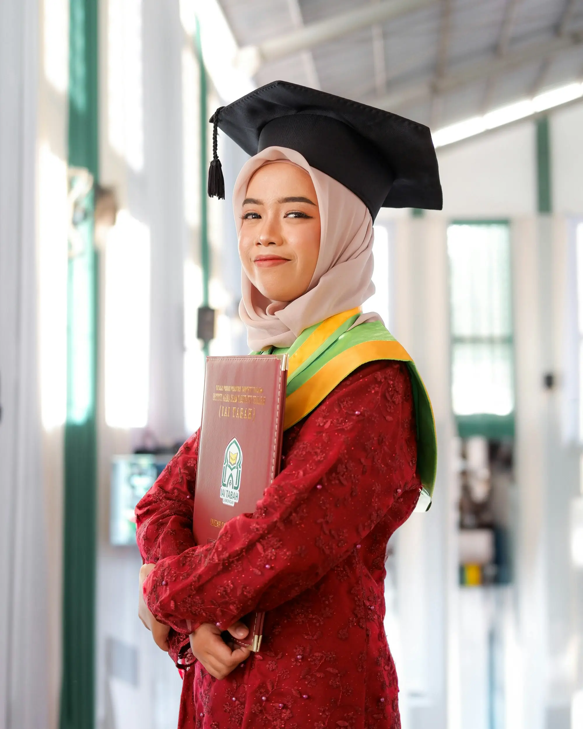 Wisudawati bertoga dan berkebaya merah memegang map ijazah