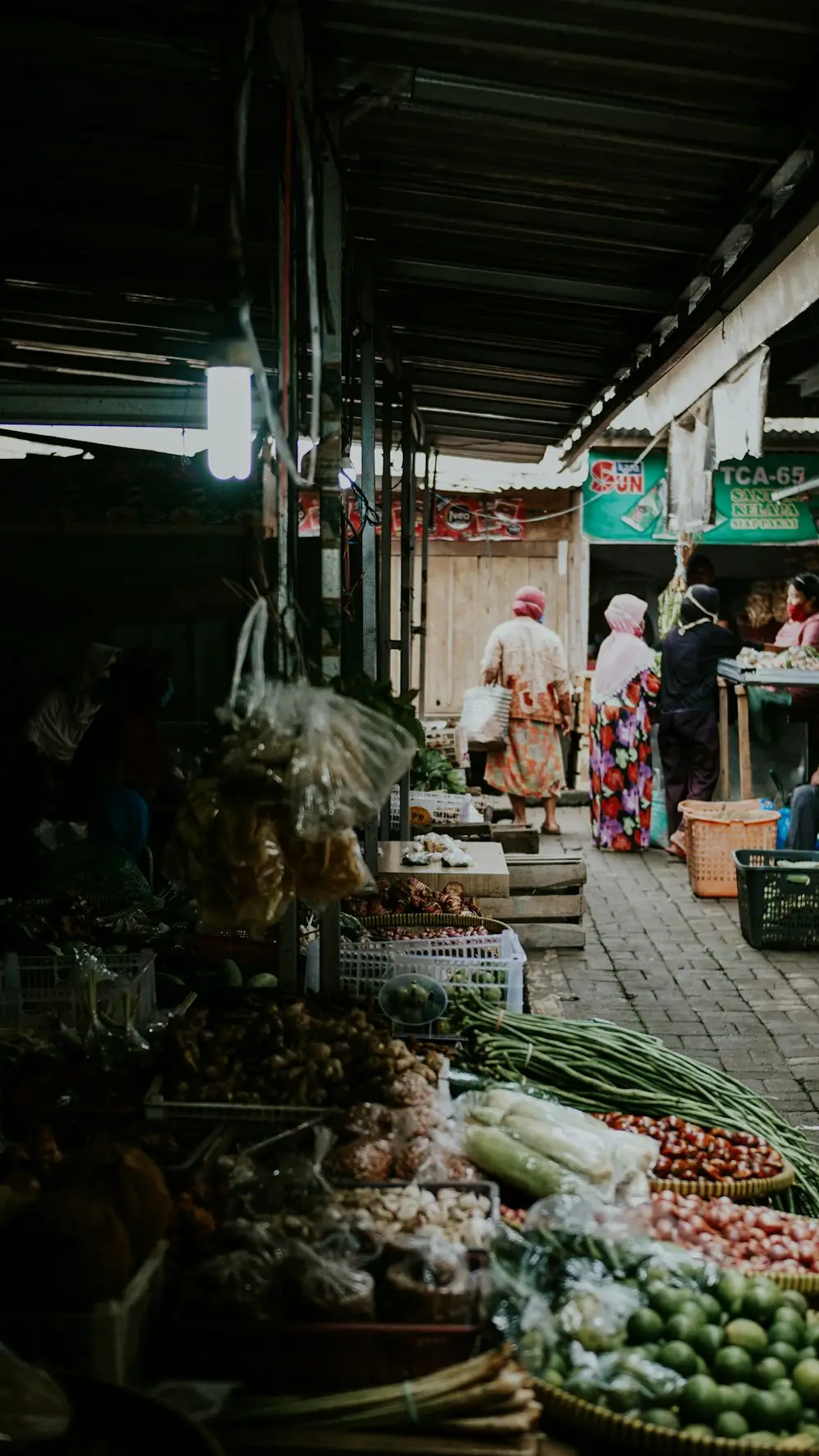 Lorong pasar pagi dengan lapak sayur di kiri dan kanan