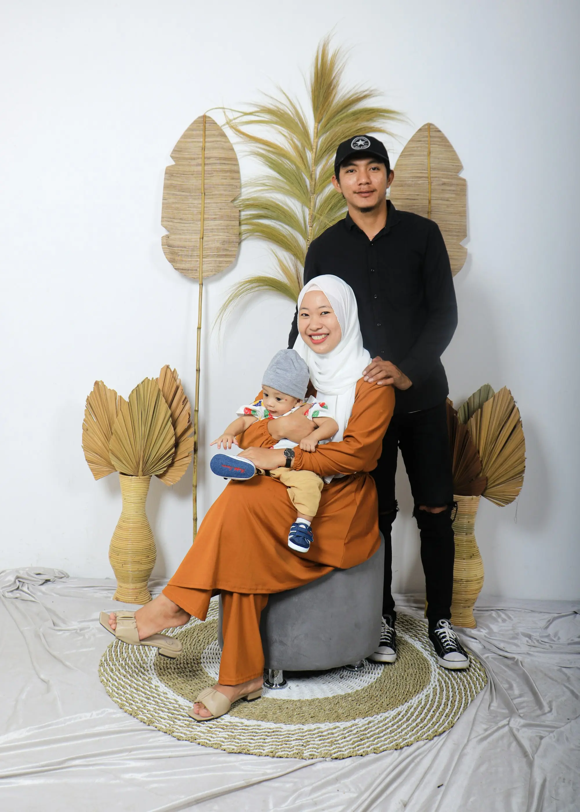 Keluarga berfoto di studio: ayah berdiri, ibu duduk memangku anak